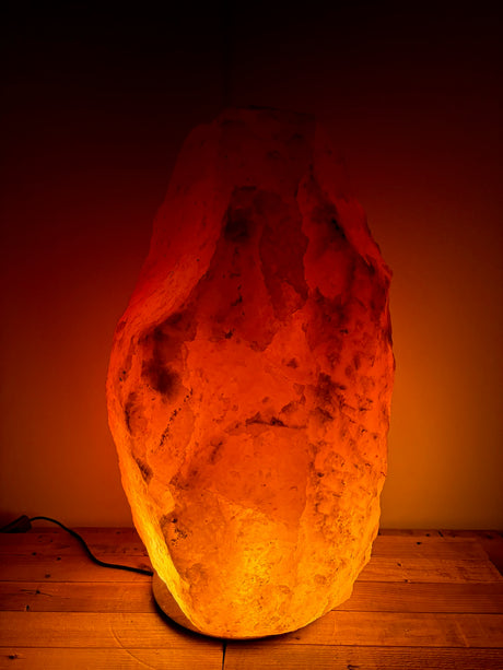 Himalaya XL zoutlamp 80–90 kg met warme amberkleurige gloed op houten voet