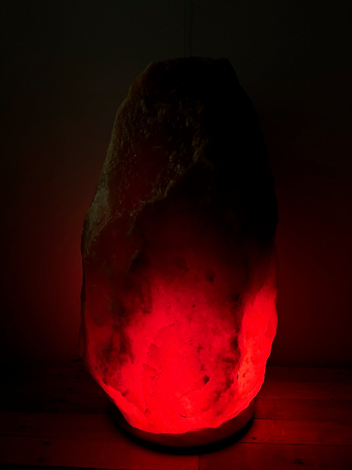 Donkere Himalaya zoutlamp 60–70 kg met warme rood/oranje gloed op stevige houten voet